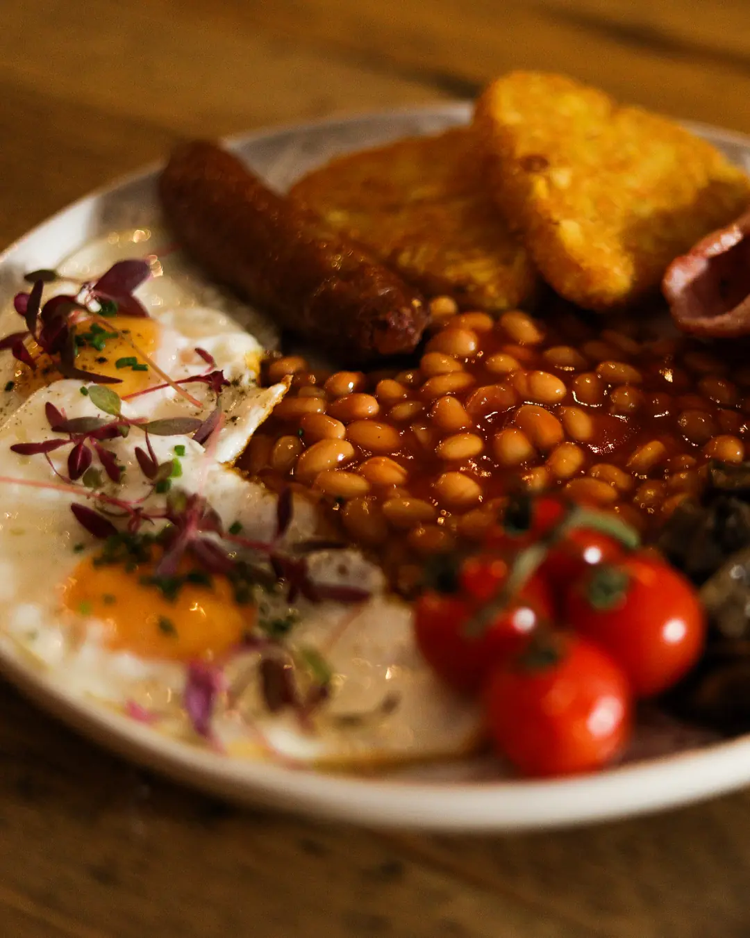 A perfectly cooked full English breakfast on a plate with sausage, bacon, and fried eggs.