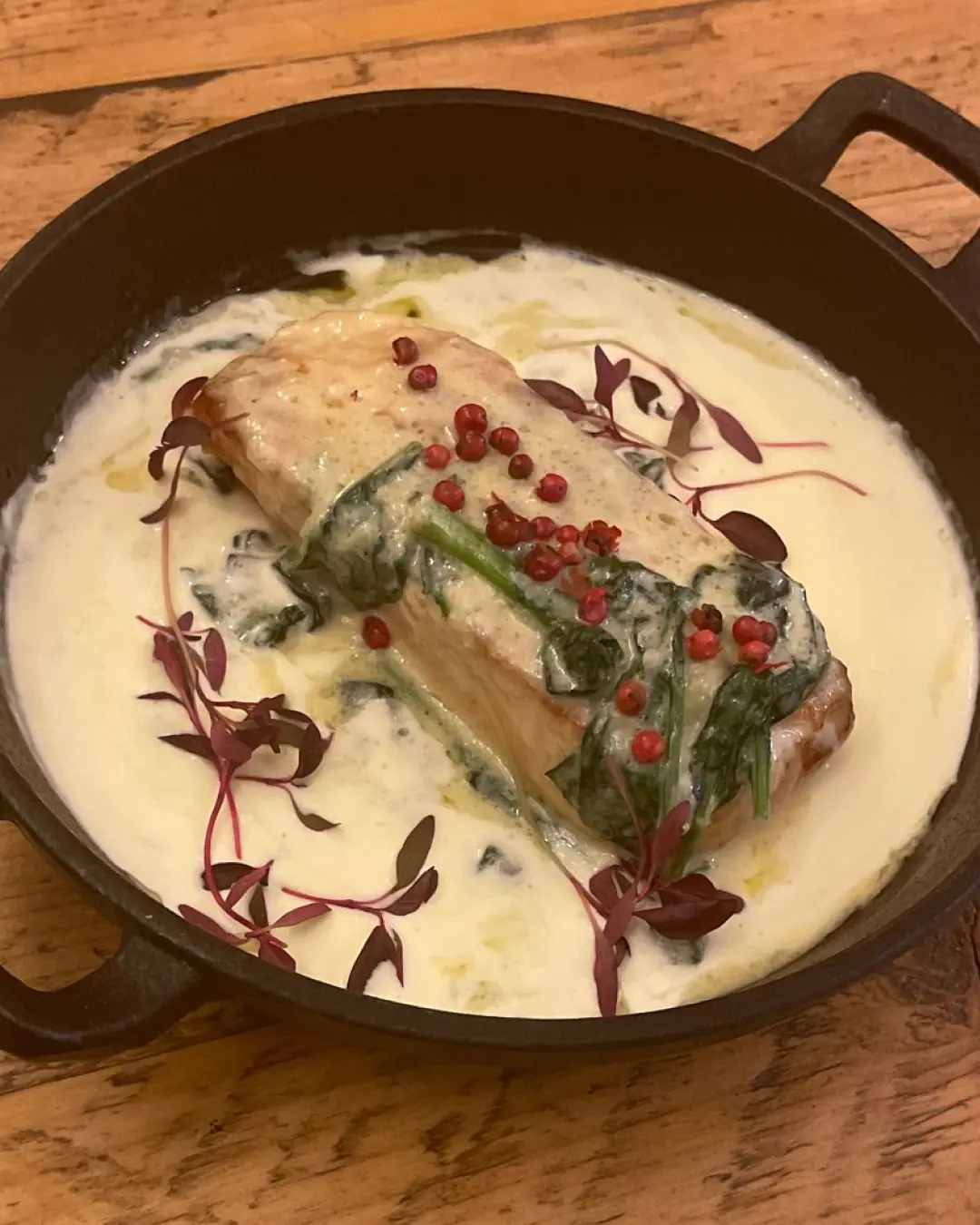 A seared salmon fillet served on a white plate with a creamy sauce and fresh herbs.
